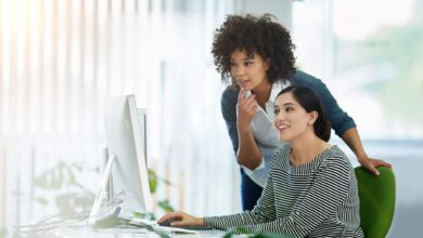 Two female coworkers smiling while discussing data on a computer