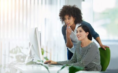 Two female coworkers in an office looking at data on a computer