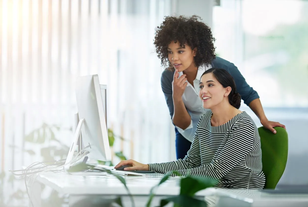 Two female coworkers in an office looking at data on a computer