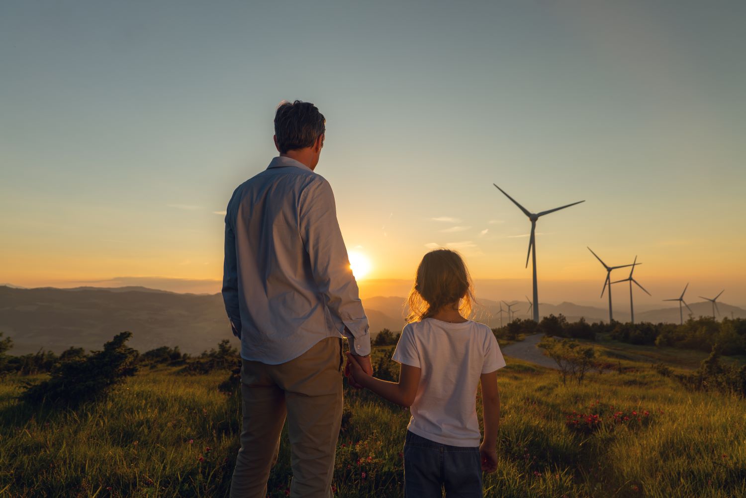 Father and child looking at sunset and wind turbines