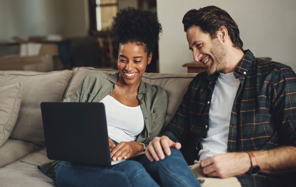 A couple on the couch smiling at a laptop on the woman's lap