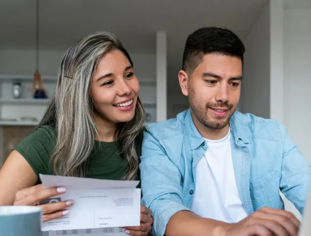 Couple smiling while looking at utility bill and laptop