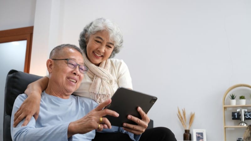 Older couple pointing and smiling at a tablet.