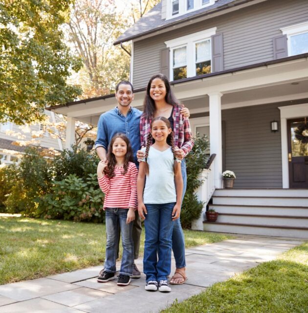 Smiling family posting on the sidewalk in front of their front porch.