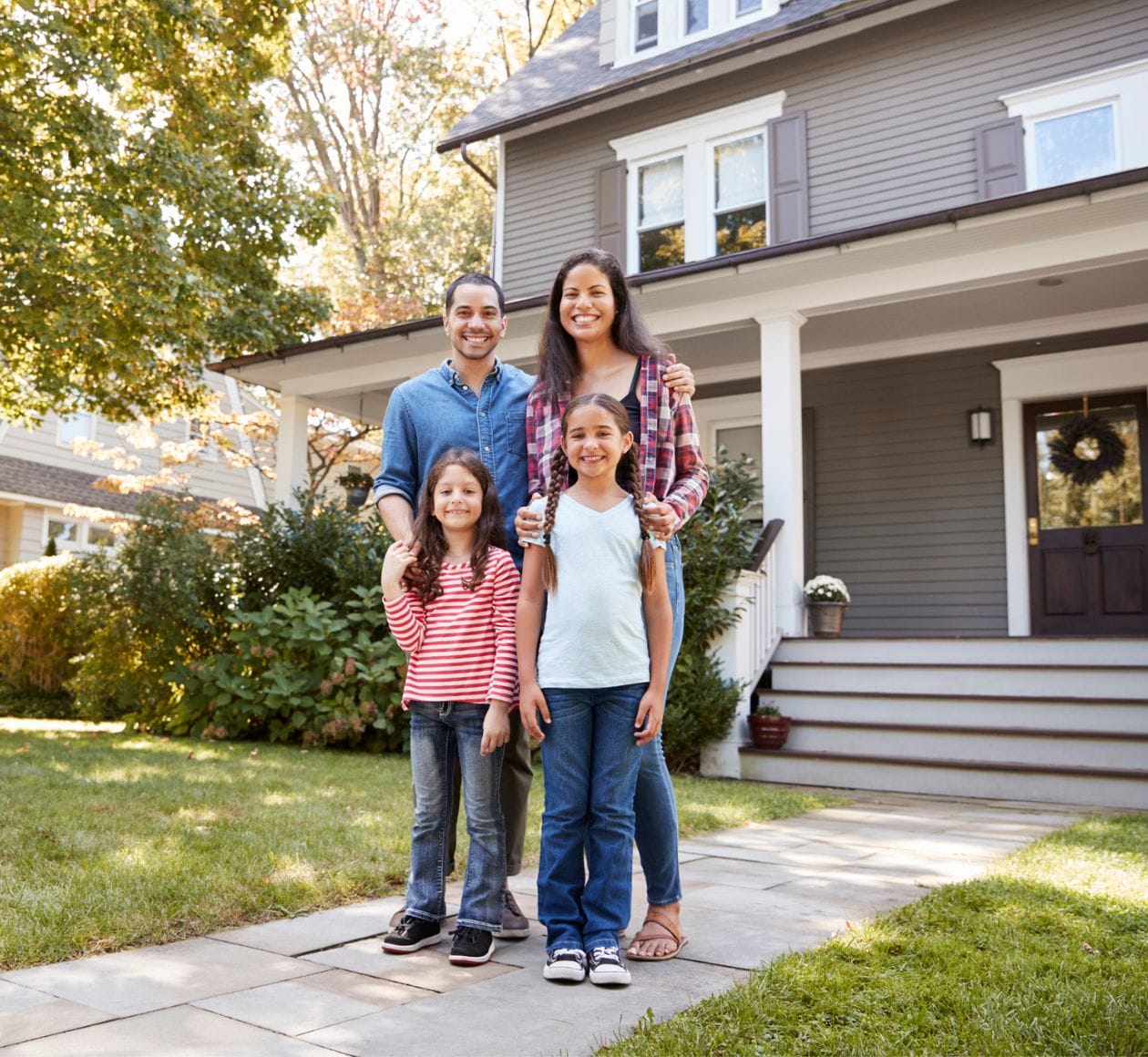 Smiling family posting on the sidewalk in front of their front porch.