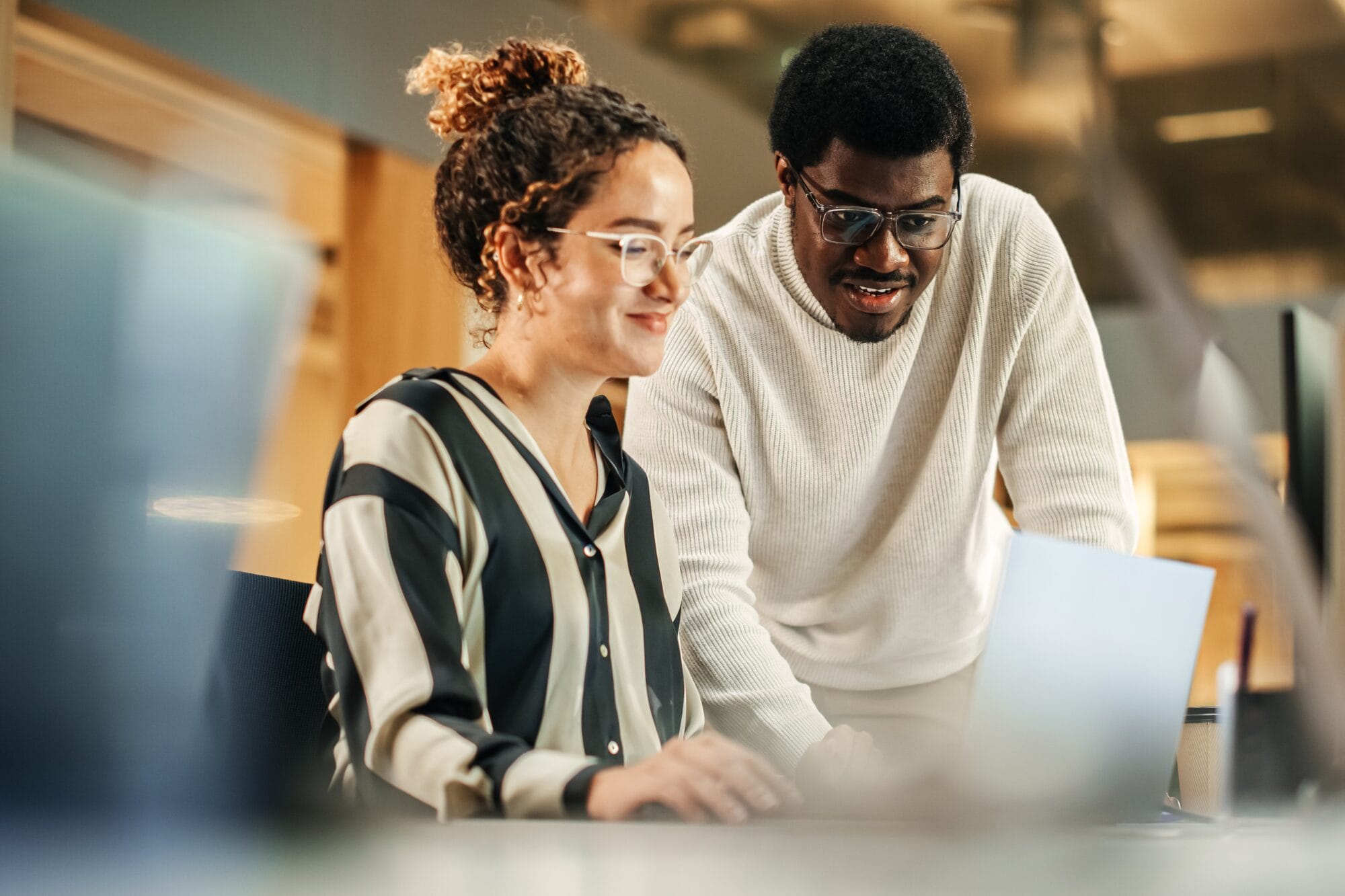 Portrait of Two Creative Colleagues Using Laptop to Discuss Work Project at Office. Young Black Technical Support Specialist Helping Female Customer Relationship Coordinator. Teamwork Concept